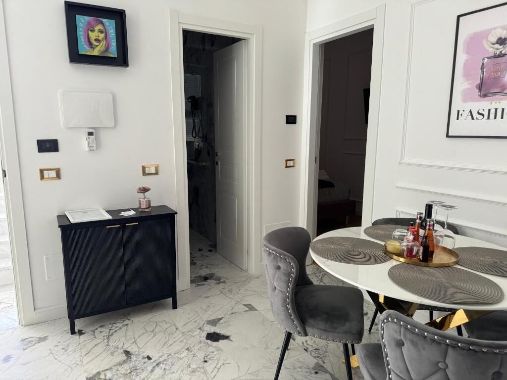 Un comedor moderno con una mesa redonda, sillas tapizadas en gris y una consola negra con una obra de arte enmarcada encima.