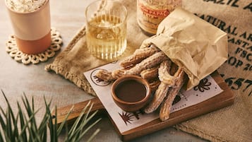 A wooden board with churros, a cup of hot chocolate, and a bottle of Coca-Cola.
