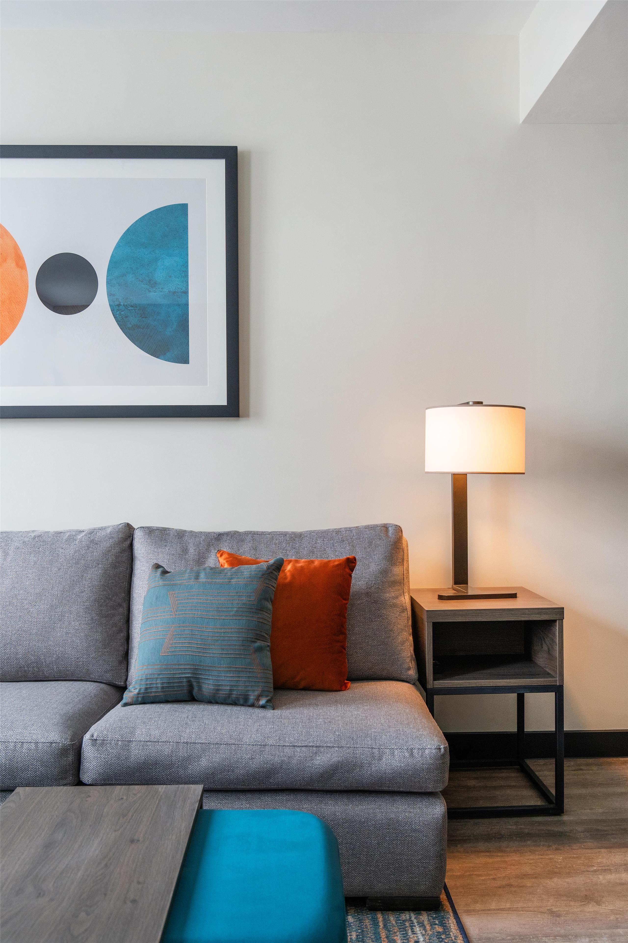 A modern living room with a grey sofa, a blue ottoman, and a floor lamp.