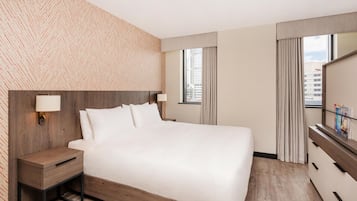 A hotel room with a large bed, bedside tables, a mirror, and a view of the city through the window.