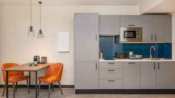 A modern kitchen with grey cabinets, a microwave, and a sink. There is a dining table with two chairs.