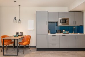 Cocina moderna con gabinetes grises, un microondas y un lavabo. Hay una mesa de comedor con dos sillas.