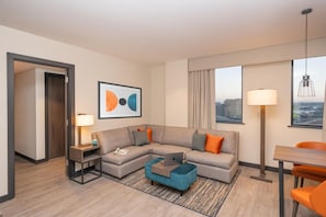 A modern hotel room with a sectional sofa, a small table, a desk, and a city view. - Hyatt House Leeds Aparthotel (Leeds)