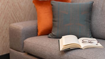 A sofa with two pillows, an open book, and a pair of glasses on it.