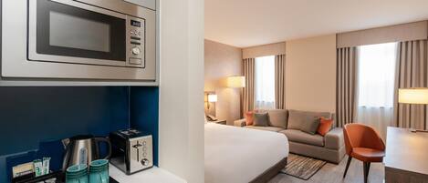 A hotel room with a bed, a sofa, a desk, a lamp, and a microwave.