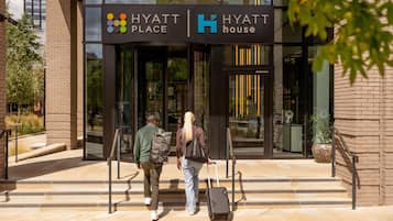 A hotel entrance with a glass facade, a sign indicating it's a Hyatt Place, and a person with a suitcase.