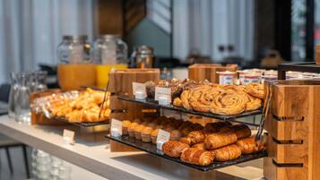 A breakfast buffet with various pastries and bread, including croissants and muffins, displayed on wooden stands.