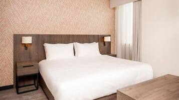 A hotel room with a large bed, two bedside tables with lamps, a wooden nightstand, and a wooden dresser.