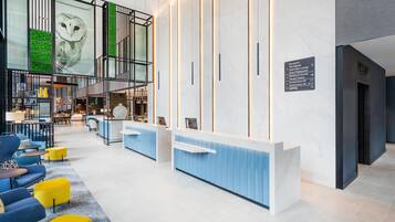 Un moderno vestíbulo de hotel con mostrador de recepción, zona de estar y un amplio muro de cristal con obras de arte.