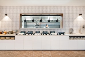 A modern kitchen with a central island, overhead lighting, and a chef preparing food. - Hyatt House Leeds Aparthotel (Leeds)