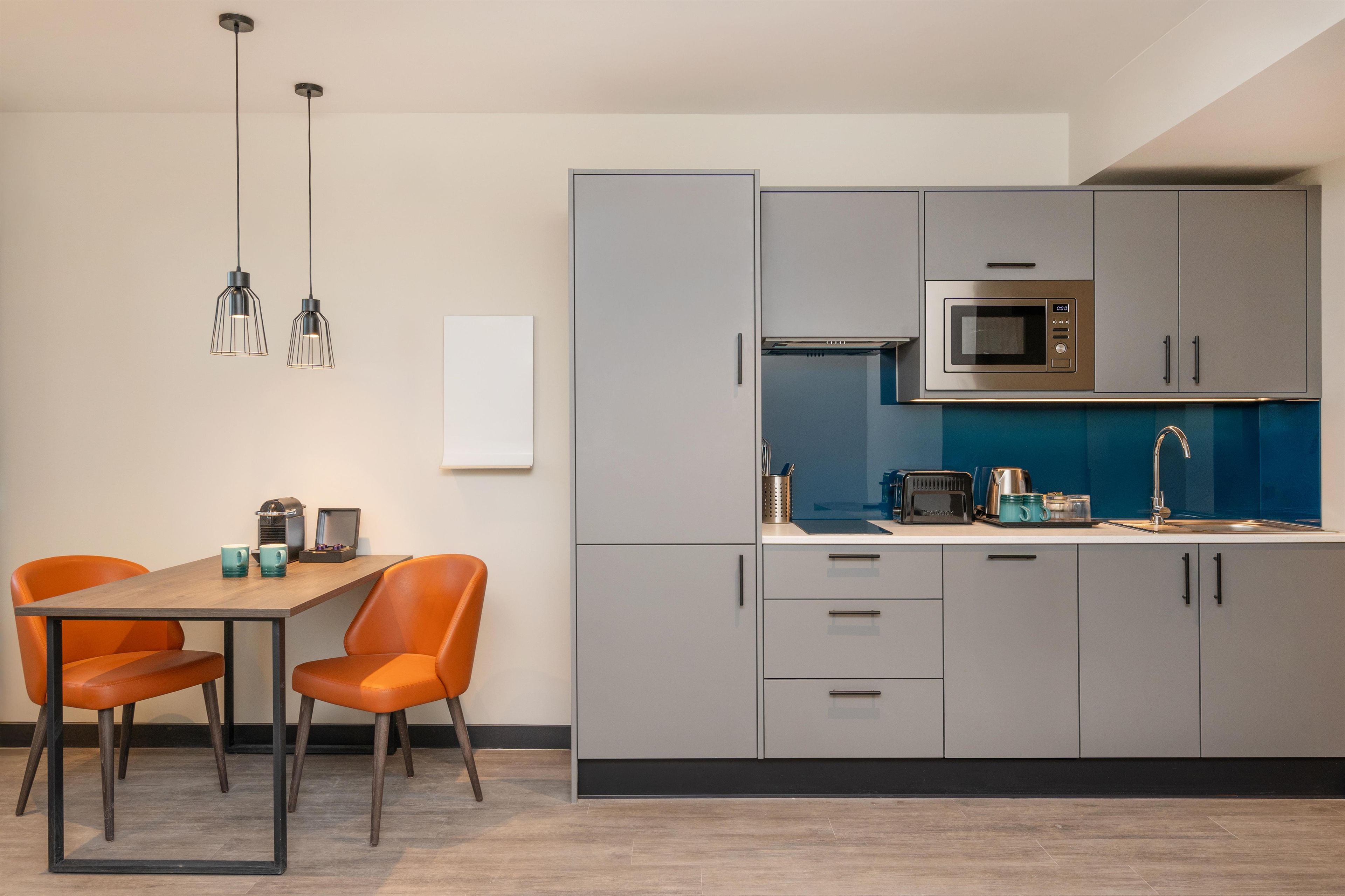 A modern kitchen with grey cabinets, a microwave, and a sink. There is a dining table with two chairs.