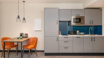 A modern kitchen with grey cabinets, a microwave, and a sink. There is a dining table with two chairs.