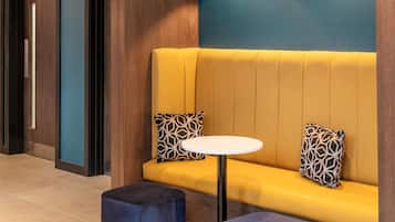 Un interior moderno con un sofá amarillo, dos cojines estampados, una mesa redonda blanca y un reposapiés azul.