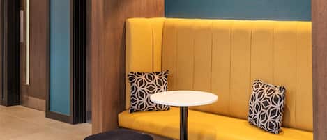 Un interior moderno con un sofá amarillo, dos cojines estampados, una mesa redonda blanca y un reposapiés azul.