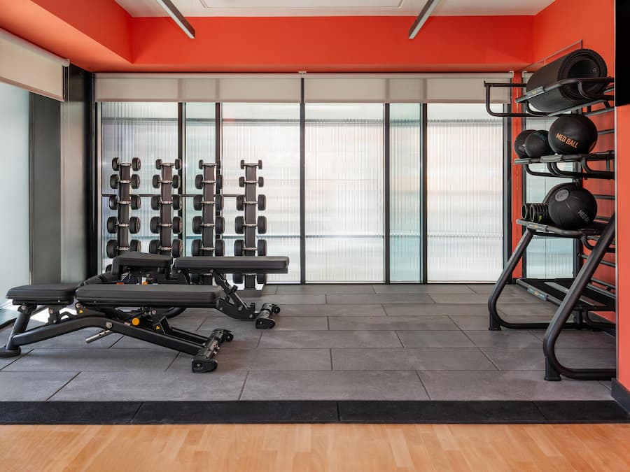 Ein Fitnessraum mit Trainingsgeräten, darunter Hanteln und eine Bank.