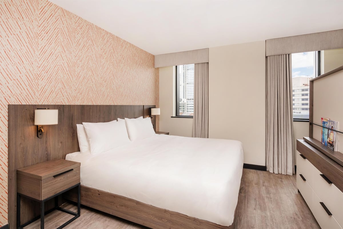 A modern hotel room with a large bed, a wooden nightstand, a dresser, and a mirror.