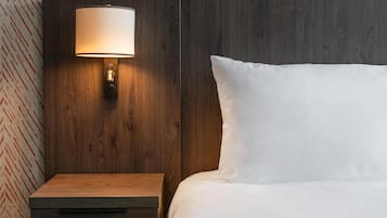 Habitación de hotel con cabecera de madera, mesita de noche con lámpara y una cama grande con ropa blanca de cama.