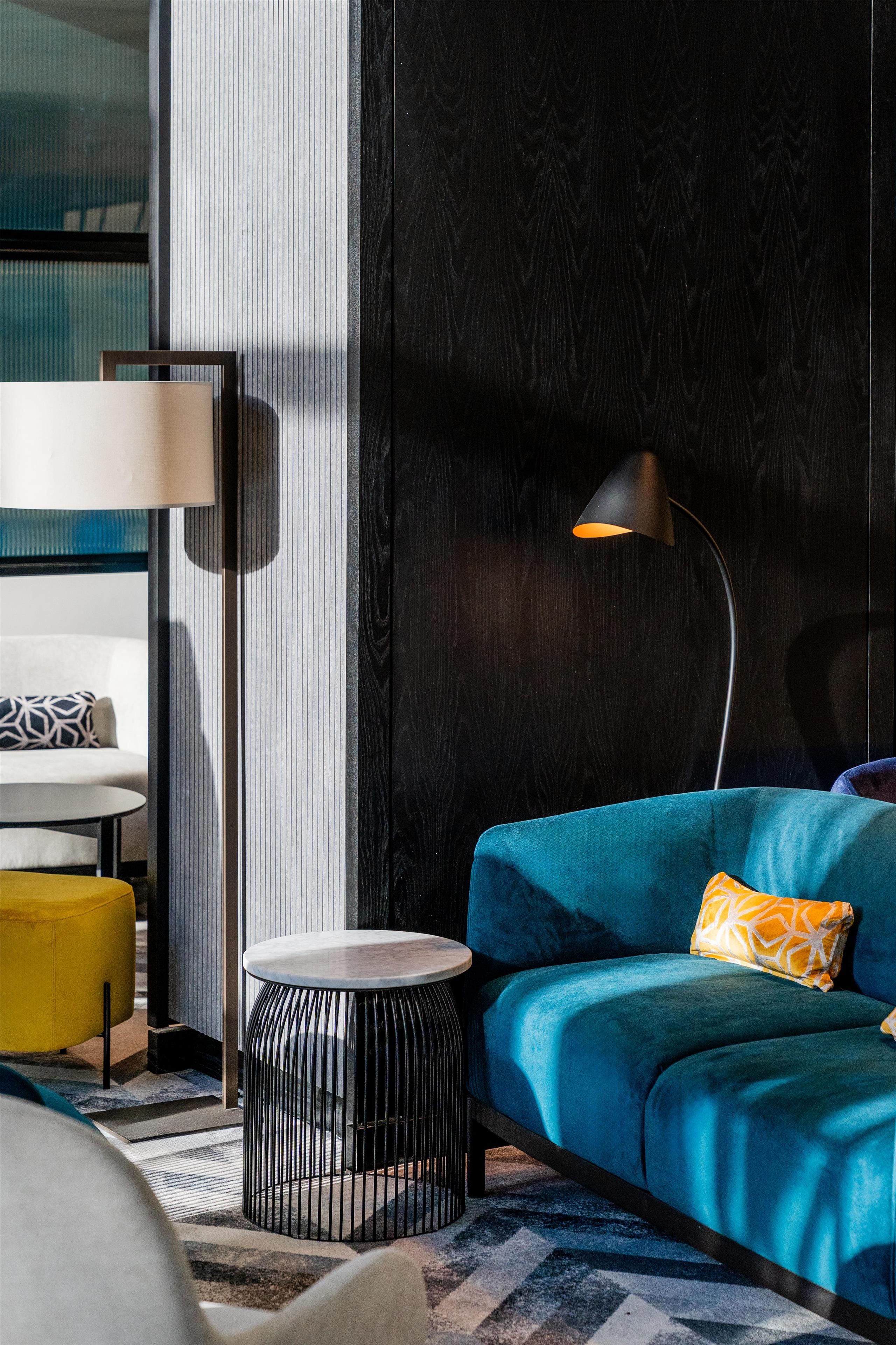 A modern living room with a blue sofa, a small round side table, a floor lamp, and a patterned rug.