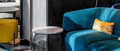 A modern living room with a blue sofa, a small round side table, a floor lamp, and a patterned rug.