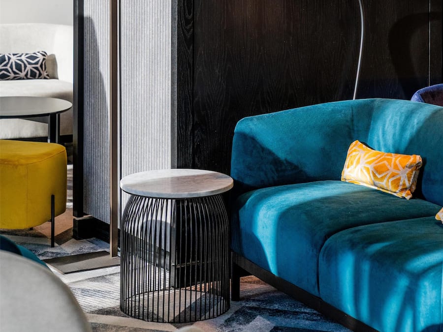 En moderne stue med en blå sofa, et rundt sofabord, en gulvlampe og en tæppe med et mønster.