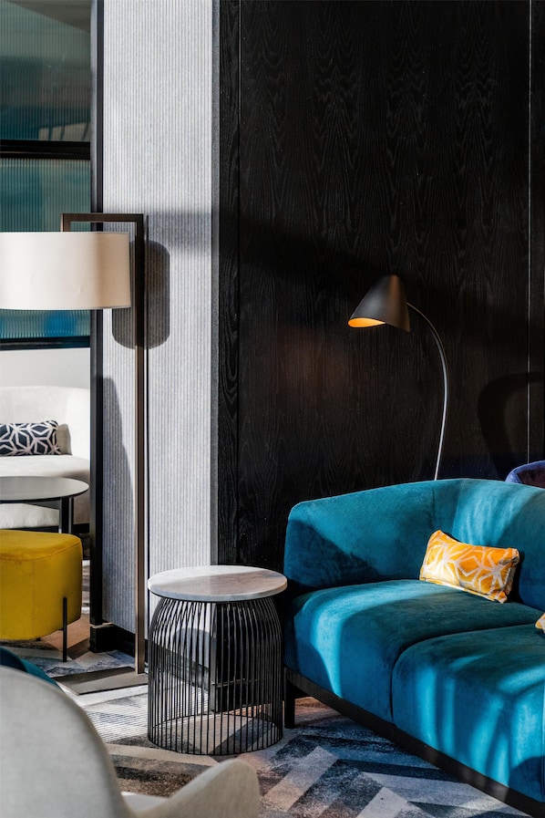 A modern living room with a blue sofa, a small round side table, a floor lamp, and a patterned rug.