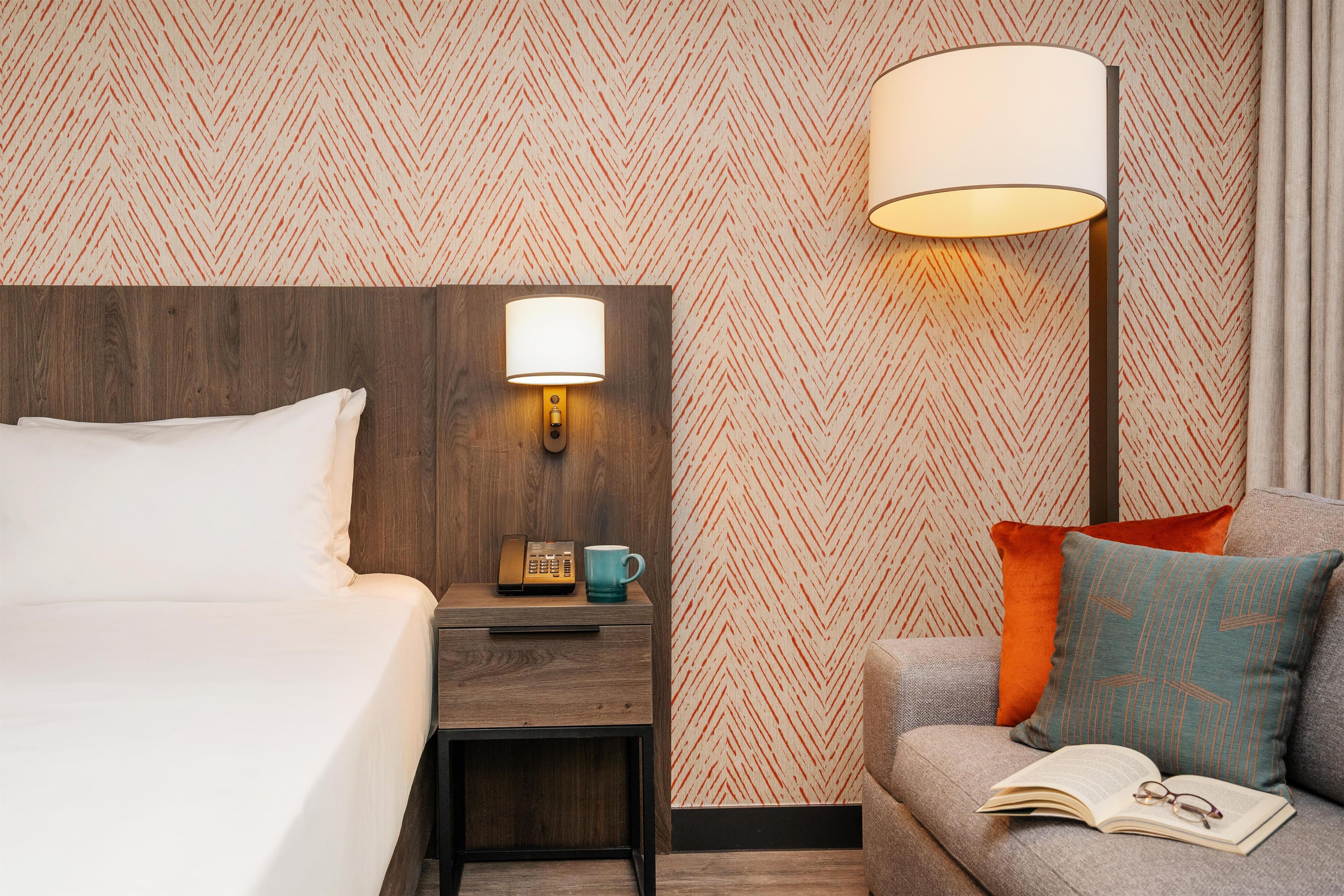 Una habitación de hotel con una cama, una mesita de noche con una lámpara, un teléfono y una taza.