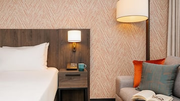 Una habitación de hotel con una cama, una mesita de noche con una lámpara, un teléfono y una taza.