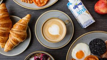 A breakfast setting with croissants, coffee, yogurt with berries, eggs, and a carton of almond milk.
