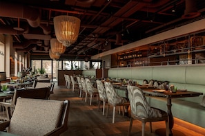 A restaurant with a long counter, cushioned seating, and hanging light fixtures. - Hyatt House Leeds Aparthotel (Leeds)