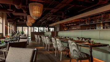 A restaurant with a long counter, cushioned seating, and hanging light fixtures.
