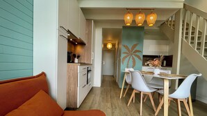 Een moderne keuken met houten kastjes, een eethoek met tafel en stoelen, en een trap naar een hoger gelegen verdieping.