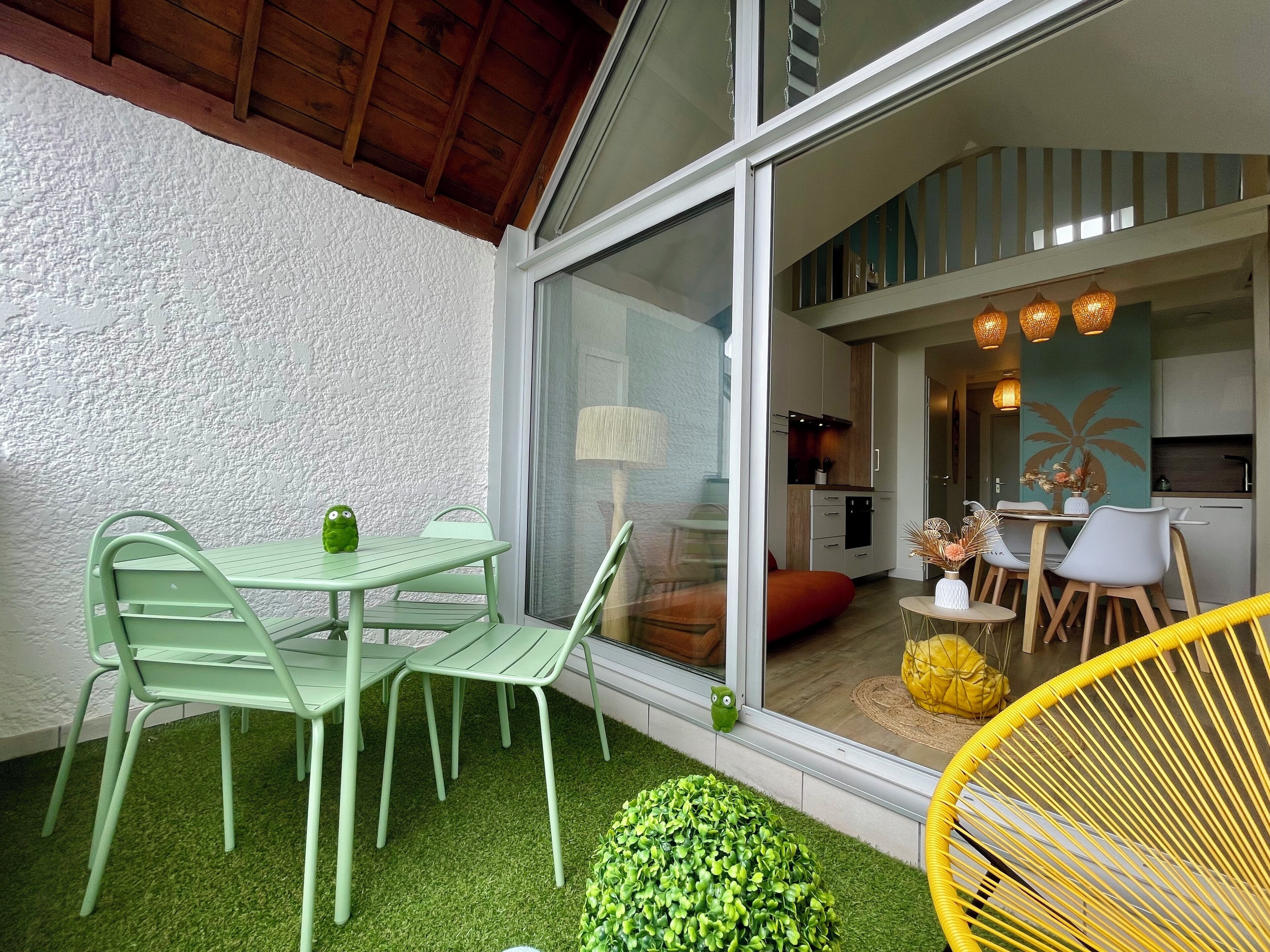 Un patio con sillas verdes, una mesita y una silla amarilla.