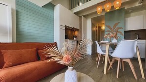 Een moderne woonkamer met een bank, een ronde salontafel met een vaas, en een eethoek met stoelen en een tafel.