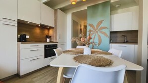 Een moderne keuken met witte kastjes, een houten aanrechtblad en een eethoek met een witte tafel en stoelen.