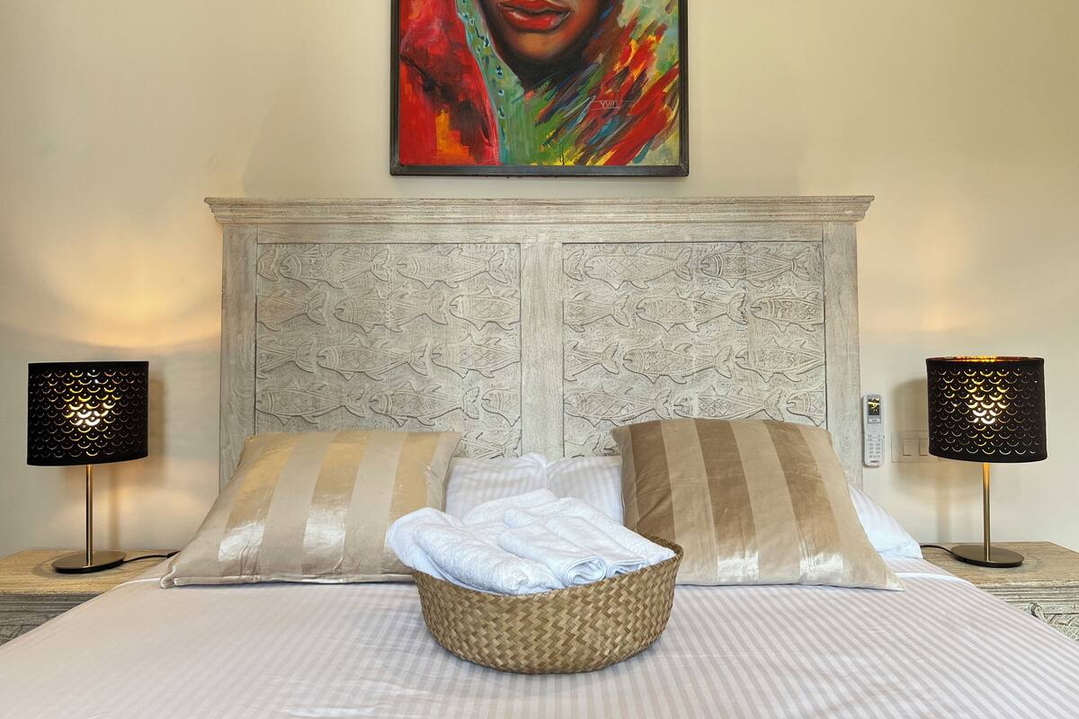 Una habitación de hotel con una cama grande, dos lámparas de noche, un cabecero decorativo y un cuadro en la pared.