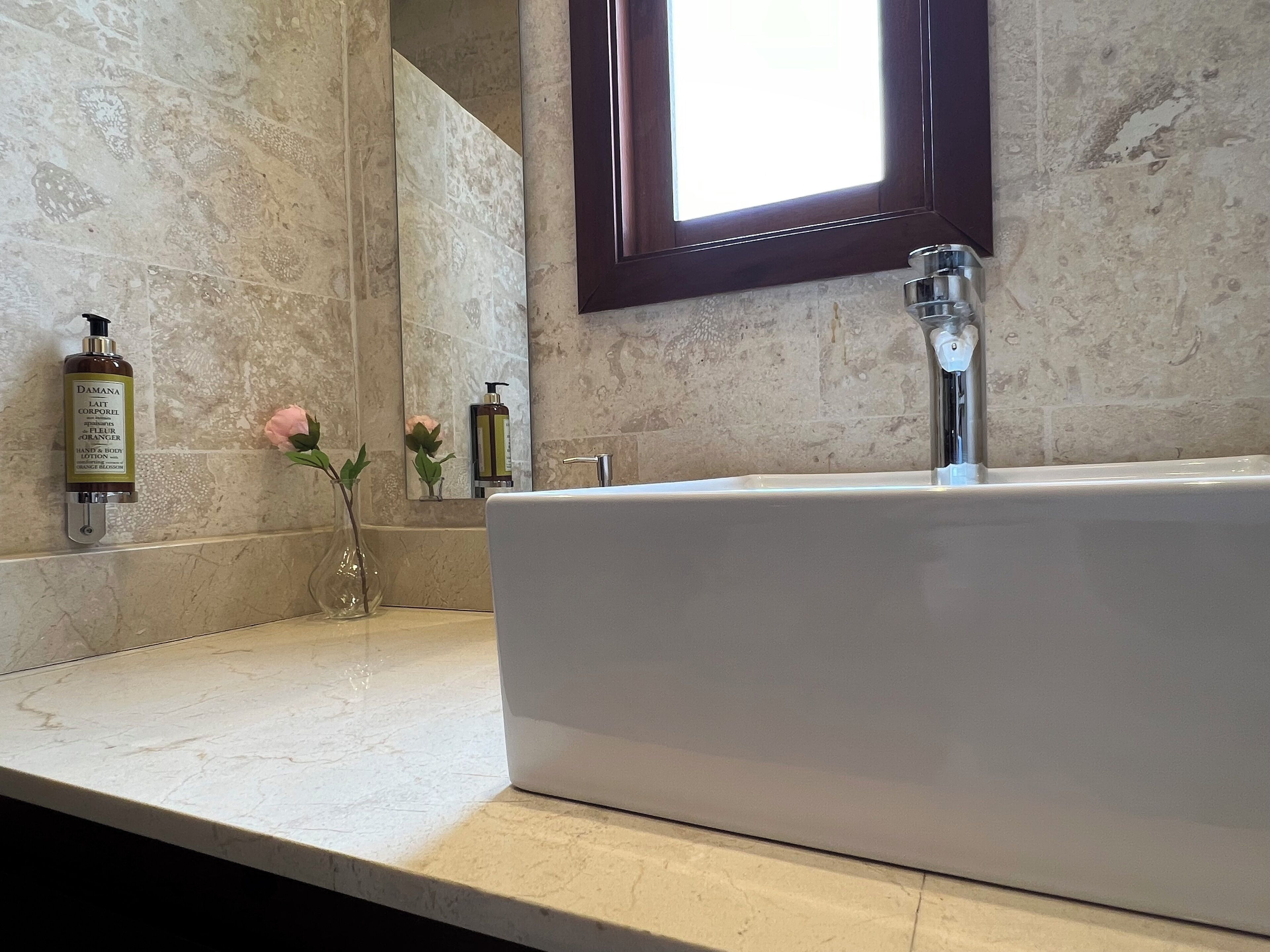 Une salle de bain avec une grande baignoire, un miroir et une fenêtre. On y trouve des articles de toilette sur le comptoir et un vase avec des fleurs.