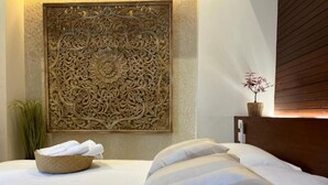 A neatly made bed with white linens and pillows, a decorative wall panel, a small plant, and a wooden headboard. - Casa Grande (Santo Domingo)