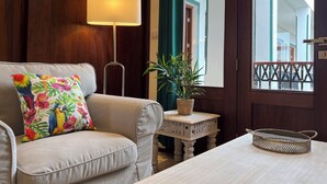 A living room with a sofa, a lamp, a small table with a plant, and a window with a view of a building. - Casa Grande (Santo Domingo)