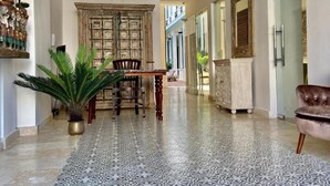 A spacious hallway with a patterned floor, a wooden dining table with chairs, a large potted plant, and a brown leather armchair. - Casa Grande (Santo Domingo)