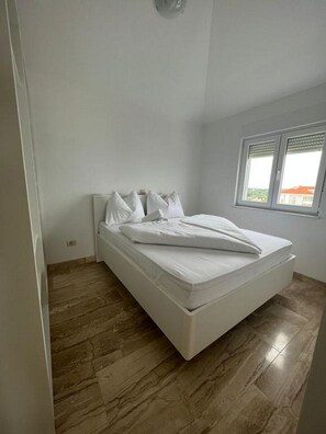 Un dormitorio con una cama individual, una ventana con persianas y suelo de madera.