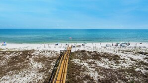 Ein Strand mit einer Holzpromenade, die zum Wasser führt, feinem Sand, Sonnenschirmen und blauem Himmel.