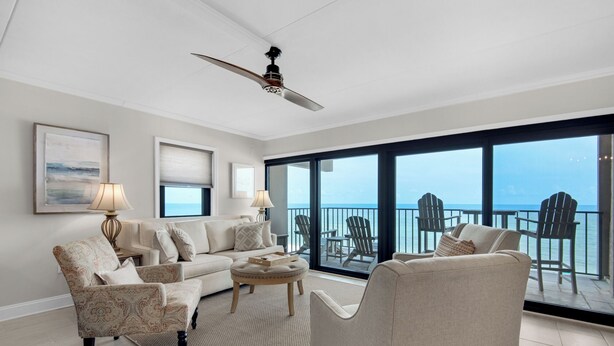 Ein geräumiges Wohnzimmer mit großem Balkon und Meerblick, ausgestattet mit Deckenventilator, bequemen Sitzgelegenheiten und Wandbildern.