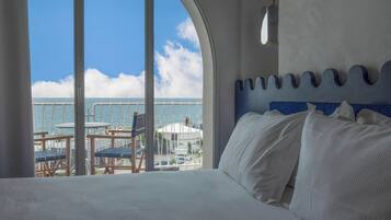 A hotel room with a large bed, a view of the sea, and a balcony with outdoor seating.