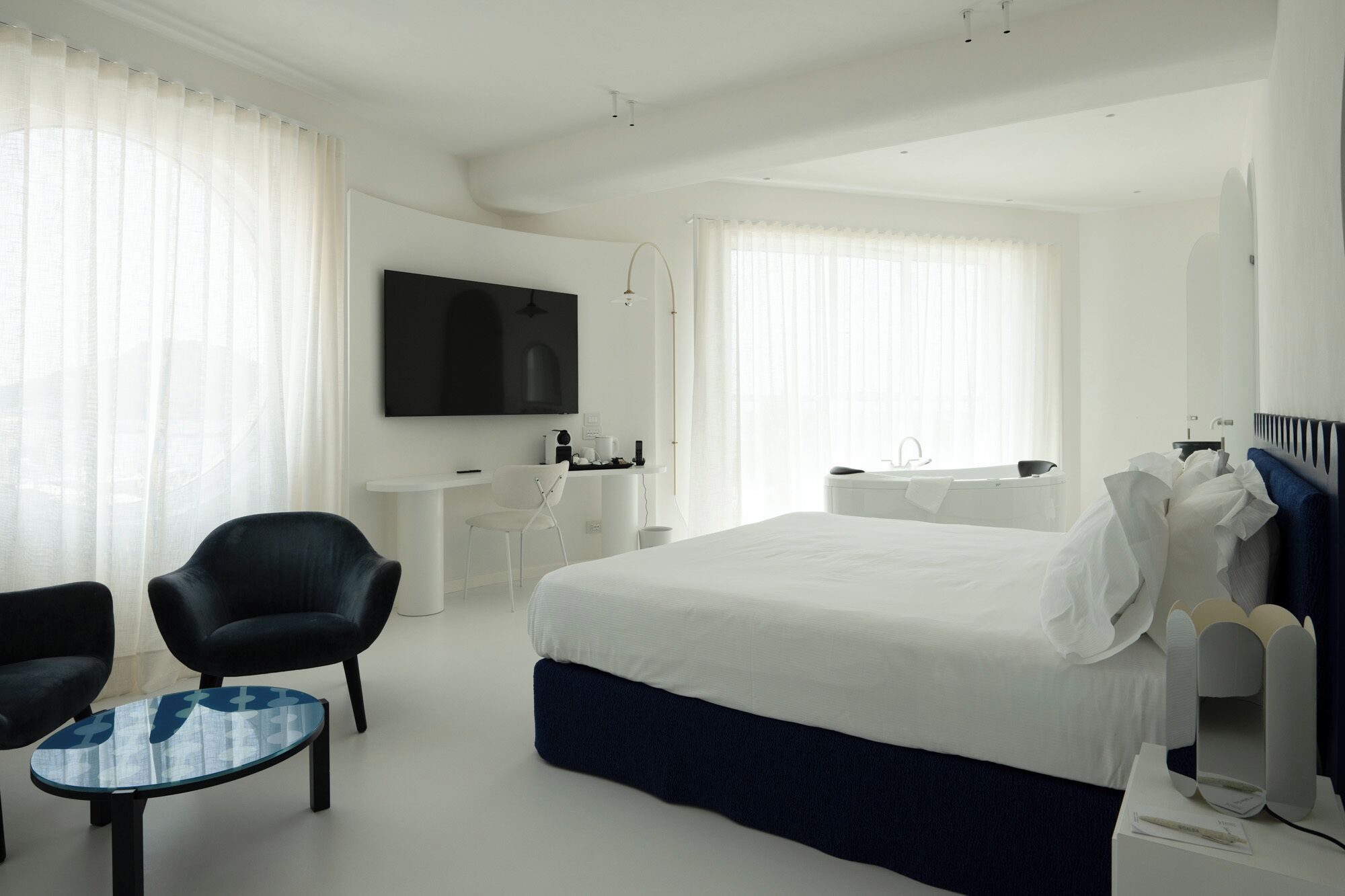 Quarto de hotel moderno com uma cama grande, uma escrivaninha, uma cadeira, uma televisão e um banheiro.