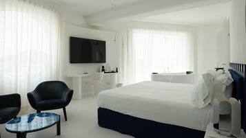 Quarto de hotel moderno com uma cama grande, uma escrivaninha, uma cadeira, uma televisão e um banheiro.