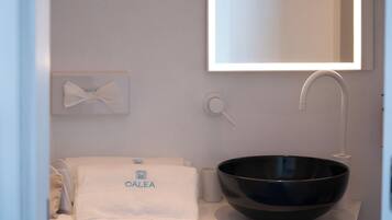 Une salle de bain avec un lavabo noir, une serviette ornée du logo « CALEA », une serviette blanche, une tasse blanche et un miroir.