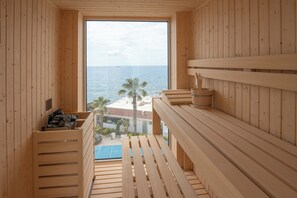 Relax in a serene ocean-view sauna with a large window and wooden benches.