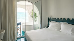 A hotel room with a bed, a chair, a table, and a view of the ocean through a glass door. - CALEA Boutique Hotel (Bacoli)