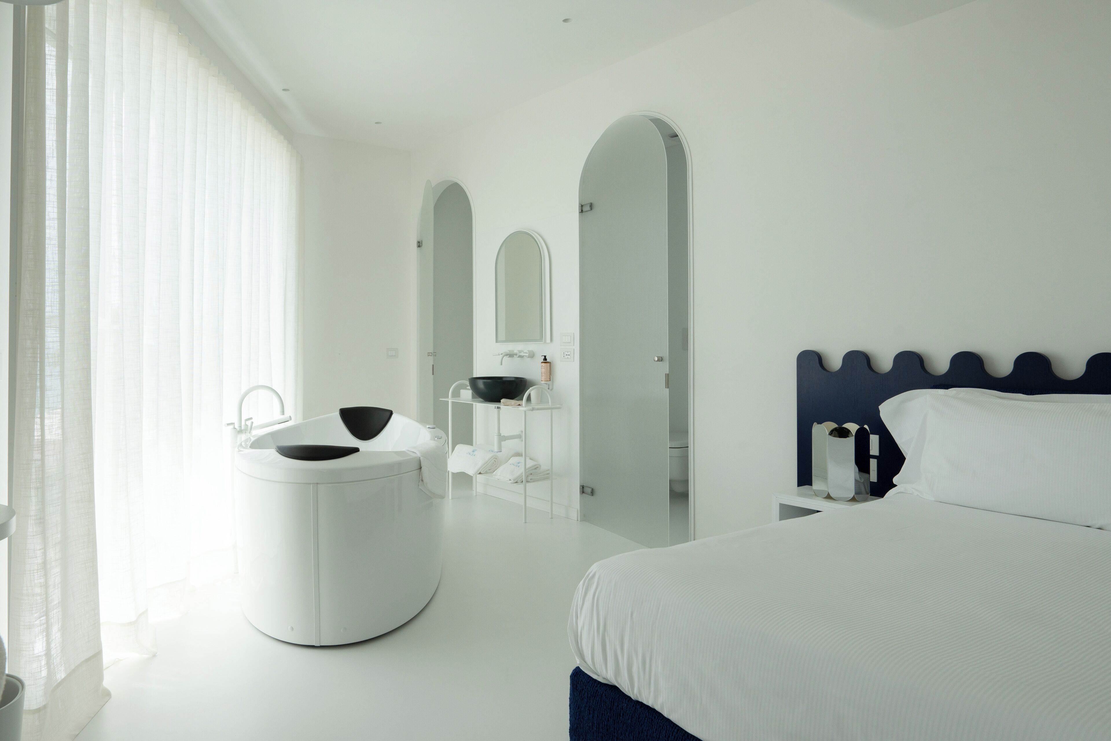 A modern hotel room with a large bed, a round vanity with a sink, and a mirror.
