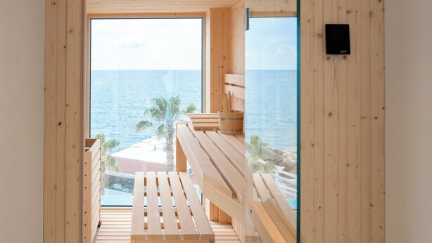 A wooden room with a bench and a surfboard, overlooking a beach with palm trees and the sea. - CALEA Boutique Hotel (Bacoli)